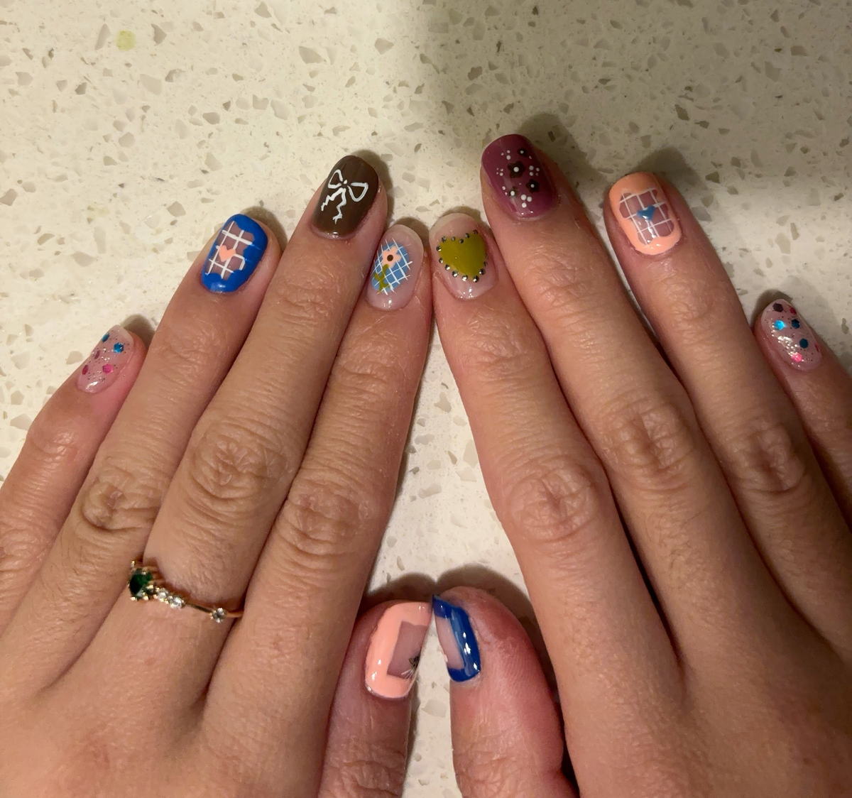 Two hands with ten different short square designs: blue plaid, a painted bow, checkerboard, a chartreuse heart and pastel confetti.