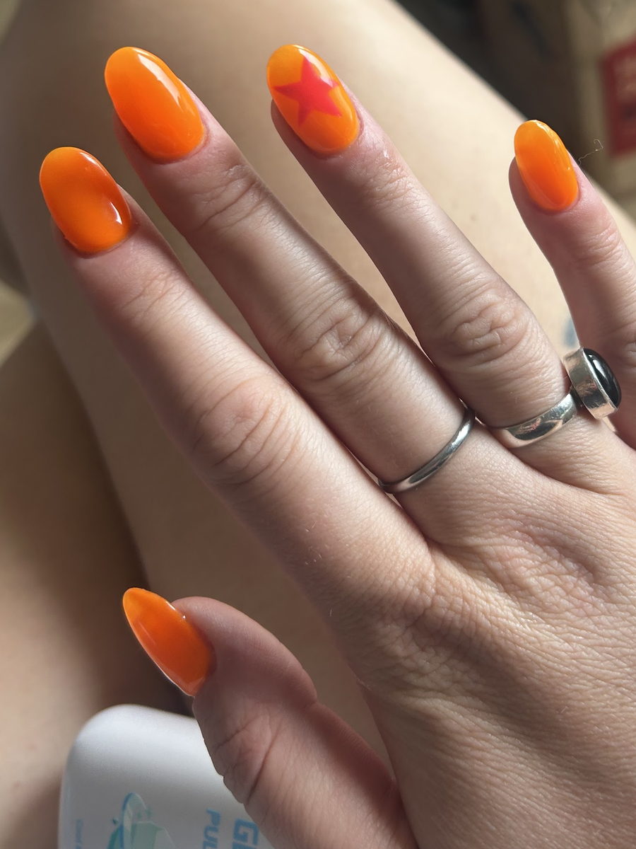 A set of glossy tangerine nails in an almond shape, one of them painted with a red star.