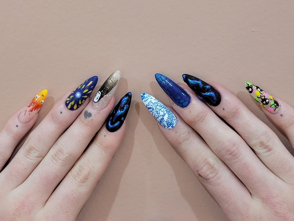 Two hands with long stiletto nails: a flame character on orange, a white masked figure over gold glitter, blue chrome and marble, a blue-and-white porcelain dragon, and small black soot sprites.