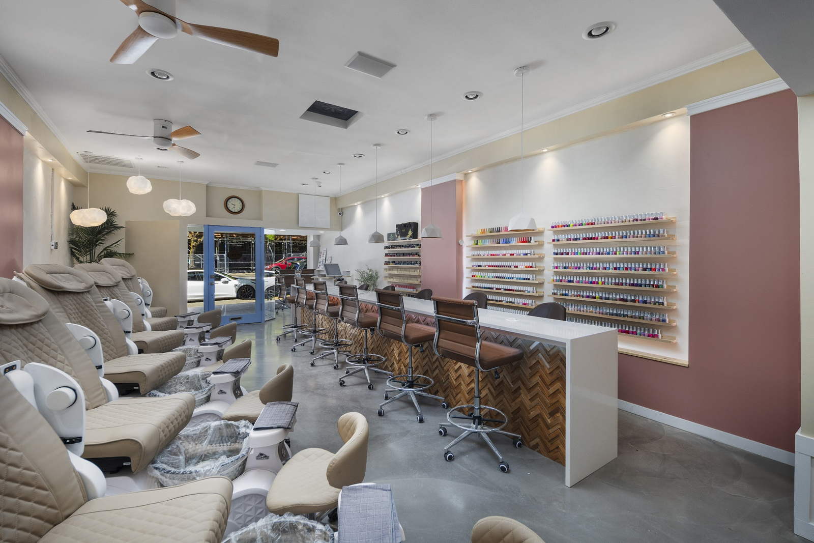 Inside Polished Perfection: pedicure chairs on the left, a long white manicure bar with herringbone paneling, and a wall of color on dusty-pink walls.